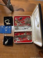 Jewelry boxes and display trays with various necklaces and pendants including heart-shaped pendants, chains with stones, and silver-tone metals.