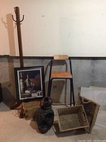 Full view of lot showing coat rack, chair, framed art, decorative vase, and two woven baskets on floor against wall