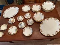 Complete view of the Royal Albert china set pieces laid out on wooden table, showcasing plates, cups, saucers, and serving pieces with floral rose pattern and gold trim.