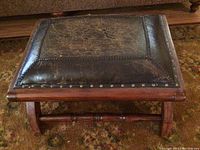 Top view of rustic ottoman showing worn, dark leather with tear and nailhead trim around the edges.