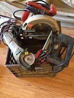 Three power tools in a black container: Skilsaw circular saw, angle grinder, and Black & Decker reciprocating saw.