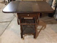 Front view of wooden tea trolley showing extended drop leaf, drawer, legs, and bottom storage shelf.