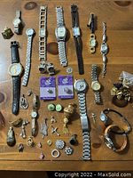 Overview showing all watches, earrings, pendants, charms laid out on wood surface.