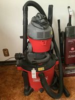 Photo showing the larger Craftsman shop vac with hose attached and power cord wrapped on top, positioned next to a smaller upright vacuum.