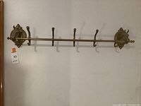 Full view of the brass horse head wall-mounted coat hanger showing five hooks and ornate horse head mounts on both ends attached to the wall.