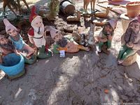 Seven gnome statues arranged outdoors on ground under tree