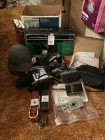 Overview photo showing metal helmet, cameras, belts, and books with manuals and camera accessories spread on carpet