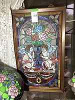 Frontal photo showing the full stained glass panel with cherubs and floral design inside a bronze frame.
