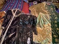 Photo showing four vintage gowns lying side by side on bed, protective plastic covering.