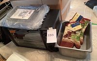 View of Ultrex toaster oven with plastic cover and large metal baking dish alongside oven mitts inside dish, showing lot contents.