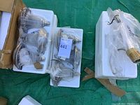 Four stainless steel solar lanterns wrapped in plastic and secured in foam inserts inside a cardboard box.