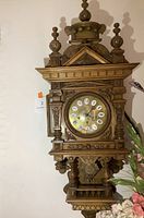 Full front view of carved wood wall clock with round brass-tone dial, finials and scrollwork