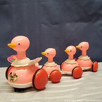 Full view of the pink duck toy set showing one large parent duck followed by three smaller ducks connected in a line. The toy appears in good condition with bright colors and clean wheels.