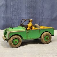 Side view of vintage green Land Rover toy showing paint wear and driver figure inside.