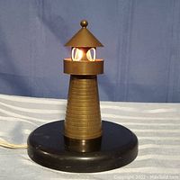 Full view of the small metal lighthouse lamp on black circular base with cord.