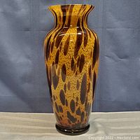 Full view of the tall art glass vase with amber and brown animal print pattern.