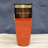 Front view of the insulated coffee cup showing the black top with white 'CHALLENGER' text and the orange body with embossed Dodge ram logo and 'DODGE' text.