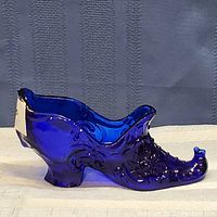 Side view of a cobalt blue translucent glass shoe figurine detailed with floral embossing and glossy finish.
