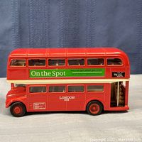 Side view of red London double decker bus model with advertising decals and open rear stairwell
