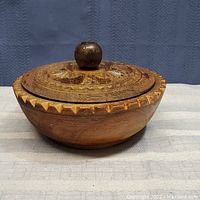 Wooden lidded dish showing carved edging and carved lid with knob handle.