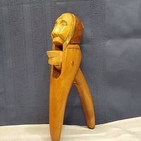 Side view of hand carved wooden nutcracker shaped like a man's head with lever for cracking nuts