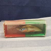 Side view of the hand painted Wobbler fishing lure inside original plastic box with painted red, white, and green backing card.