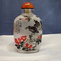 Front view of glass scent bottle showing hand-painted birds, flowers, and Chinese characters with carnelian lid on top.