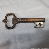 Full length image of vintage key-shaped metal tool on white textured fabric background