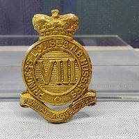 Front view of gold-colored metal cap badge with crown and Roman numeral VIII, and inscriptions showing Princess Louise's N.B. Hussars and Regi Patriaeque Fidelis.