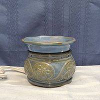 Side view of blue-gray ceramic wax melting pot with decorative floral and swirl patterns, electric cord visible.