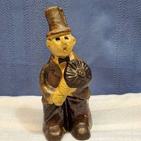 Front view of the figurine showing the full body with a top hat, bow tie, and the round object held in both hands.