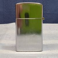 Front view of the vintage silver tone cigarette lighter showing vertical grooves and flip-top lid in reflective silver tone metal.