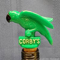 Close-up of green plastic Corby's parrot bottle stopper with white CORBY'S lettering and cork base.