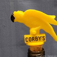 Close-up of yellow bird-shaped bottle stopper with 'CORBY'S' label on base and cork bottom visible.