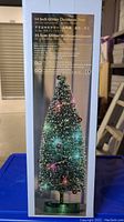 Side panel of Christmas tree box showcasing 14 inch glitter tree with LED lights and decorations, listing product details in multiple languages.
