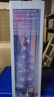 Photo of the product packaging box showing a picture and details of a 14 inch glitter Christmas tree with battery powered LED lights, labeled in several languages and with brand and safety information.