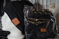 One black fleece-lined Bluetooth toque on a mannequin head and one identical toque in plastic packaging