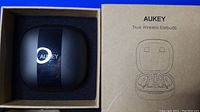 Black Aukey wireless earbuds charging case in open box with Aukey brand packaging visible.