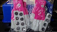Two pairs of pink and white battery powered heated gloves still sealed in plastic packaging with detachable replacement batteries visible.