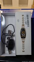Smart watch with silver and gold metal band displayed in box alongside matching box featuring image of the watch.