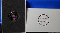 Silver smart watch with round spherical glass display, metal adjustable band, placed in black foam insert next to white box labeled 'smart watch'.