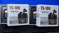 Two boxed sets of TS-100 Graffiti Design wireless earbuds visible in the image, showing the earbuds and charging cases with black and gold graffiti patterns on the packaging and cases.