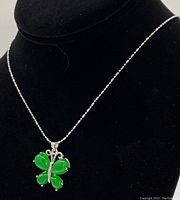 Green jade butterfly pendant on 925 sterling silver chain displayed on a black stand.