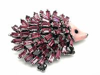 Front angled view of the hedgehog brooch showing pink enamel face and purple-pink rhinestone crystals on the body shaped like spines.