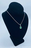 Photo of the green jade caged pendant on a snake link silver chain displayed on a black necklace stand.