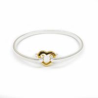 Front view of the silver plated bangle bracelet with centered gold tone heart clasp, showing its minimalistic design and clasp mechanism.