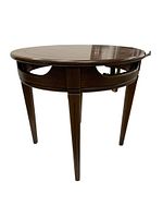 Side angle view of the round wooden side table showing tapered legs and open spaces under the tabletop.