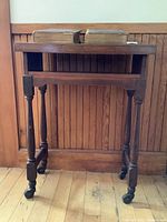 Wooden book display stand with turned legs and casters shown from front, supporting the two Dickens volumes on top.