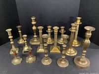 Wide shot showing entire collection of 15 brass candle holders with varied heights and styles