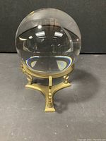 Crystal ball sitting in brass stand on black background. Ball is clear and highly polished, reflecting room light.